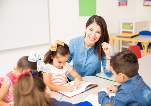 A smiling teacher next to a young girl drawing in Childcare in Peoria IL