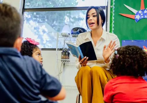 A teacher reads to preschool children. Modeling the action of reading is one of the tenants of Don Holdaway’s Foundations of Literacy.