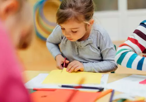 A preschool girl practices cutting paper. For anyone asking "What are Gross Motor Skills" working with scissors can help a child practice those skills.