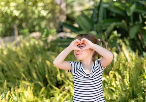 A girl holds her hands up like a heart to show gratitude, which is a way you can start Teaching Kids Good Manners from a young age